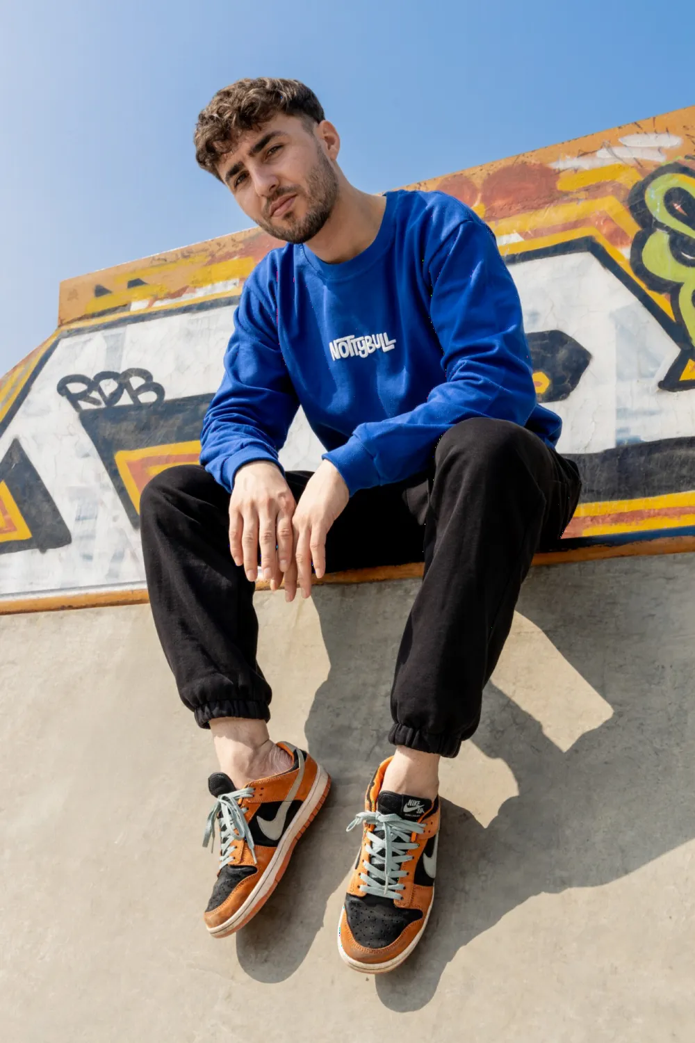 Model sitting on a graffiti wall in the royal blue NottyBull sweatshirt