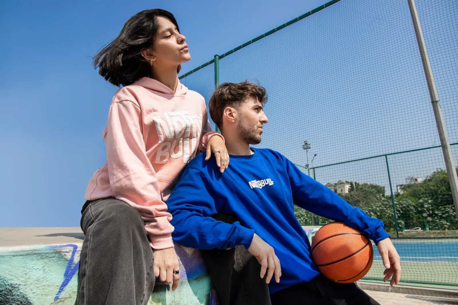 Two models on a basketball court in the pink hoodie and royal blue sweatshirt