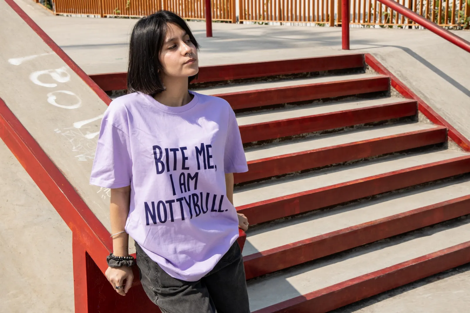 Model in the lilac Bite Me tee leaning on red skate-park stairs