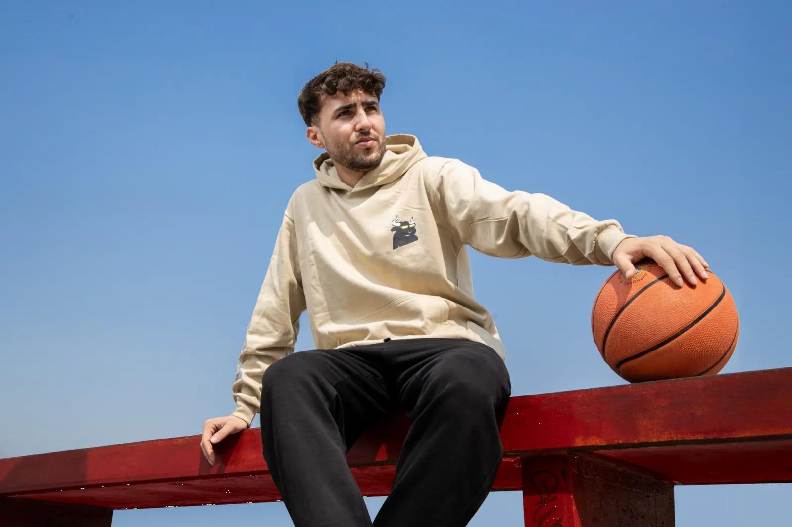 Model in a sand hoodie sitting on a red rail with a basketball